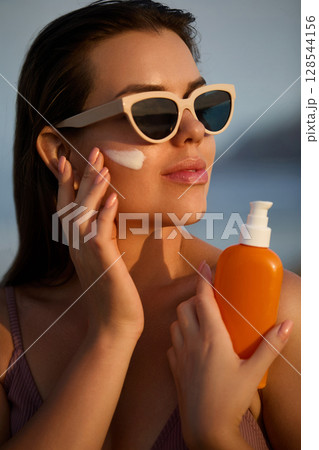 Woman Applying Sunscreen While Outdoors on a Sunny Day 128544156