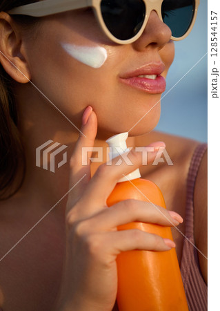 Suntan lotion woman applying sunscreen solar cream. Beautiful happy cute girl applying cream to skin. Portrait of a female holding lotion or moisturizing sun cream Suntan lotion woman applying sunscreen solar cream. Beautiful happy cute girl applying cream to skin. Portrait of a female holding lotion or moisturizing sun cream 128544157