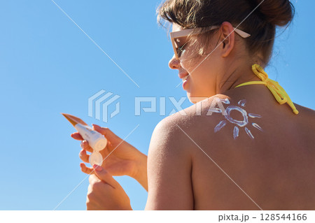 Beauty Woman applying sunscreen  on tanned shoulder. Skincare. Body Sun protection suncream. Portrair of female applying moisturizing sunscreen lotion on back 128544166