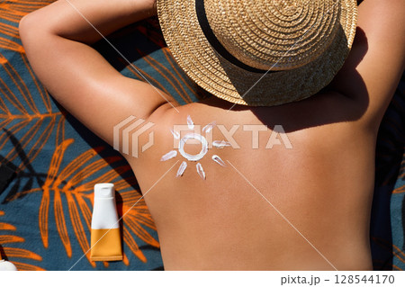 Woman Applying Sunscreen on Tanned Shoulder in Form of the Sun. Sun Protection. Skin and Body Care. Girl Putting Sun Cream on Skin. Female Holding Suntan Lotion or Moisturizing Sunblock 128544170
