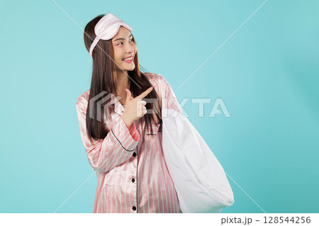 Young asian woman in pajama, sleep mask holding pillow, and smiling to point up toward an idea while at home and relaxing, she is pointing to an area for your ad, headshots isolated blue background Young asian woman in pajama, sleep mask holding pillow, and smiling to point up toward an idea while at home and relaxing, she is pointing to an area for your ad, headshots isolated blue background 128544256