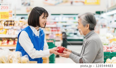 高齢のお客様にリンゴを渡す親切な女性店員 128544483