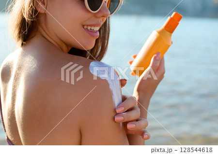 Beautiful Woman apply Sun cream on tanned back. Skin and Body Care.Sun protection. Portrait of Female in Bikini using moisturizing sunscreen lotion and Sunblock. Girl Holding Suntan Lotion Beautiful Woman apply Sun cream on tanned back. Skin and Body Care.Sun protection. Portrait of Female in Bikini using moisturizing sunscreen lotion and Sunblock. Girl Holding Suntan Lotion 128544618