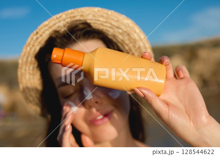 Woman smile applying sun cream on face. Skincare. Body Sun protection. sunscreen. Female in hat smear moisturizing lotion on skin. 128544622
