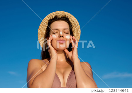 Woman applying sunscreen to protect herself from the sun during vacation. The young woman puts sunscreen on her skin to protect herself from sunburn. 128544641