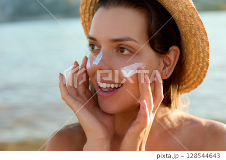 Suntan lotion woman applying sunscreen solar cream. Beautiful happy cute woman  applying suntan cream to her nose 128544643
