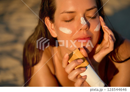 Skin care. Beauty Concept. Young pretty woman applying suncream and touch own face. Female smears sunscreen lotion on skin. Skin Protection and dermatology. Skin care. Beauty Concept. Young pretty woman applying suncream and touch own face. Female smears sunscreen lotion on skin. Skin Protection and dermatology. 128544646