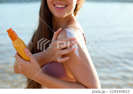 Beautiful Woman in Bikini Applying Sun Cream on Tanned Shoulder. Sun Protection. Skin and Body Care. Girl Using Sunscreen to Skin. Portrait Of Female Holding Suntan Lotion orMoisturizing Sunblock Beautiful Woman in Bikini Applying Sun Cream on Tanned Shoulder. Sun Protection. Skin and Body Care. Girl Using Sunscreen to Skin. Portrait Of Female Holding Suntan Lotion orMoisturizing Sunblock 128544652