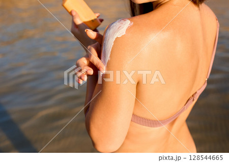 Young beautiful woman applying sunscreen on herself to protect her skin from the sun at the beach. Young beautiful woman applying sunscreen on herself to protect her skin from the sun at the beach. 128544665