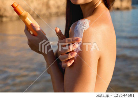 Sunscreen on tanned shoulder. Sun protection. Beautiful woman in bikini applying solar cream. Skin and body care. Portrait of female holding suntan lotion or moisturizing sunblock. Sunscreen on tanned shoulder. Sun protection. Beautiful woman in bikini applying solar cream. Skin and body care. Portrait of female holding suntan lotion or moisturizing sunblock. 128544691