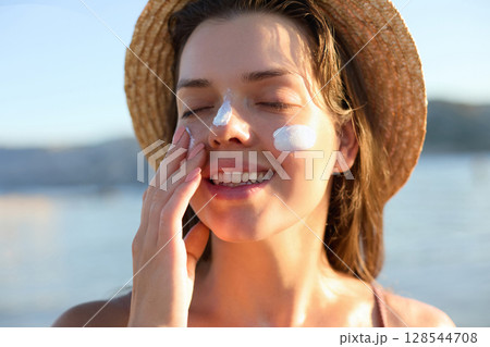 Beautiful young woman with sun cream on face. Girl applying sunscreen lotion on skin.Skin care. Sun protection. Suntan Beautiful young woman with sun cream on face. Girl applying sunscreen lotion on skin.Skin care. Sun protection. Suntan 128544708