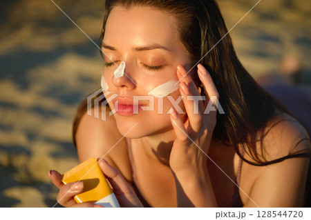 Skin care. Sun protection. Woman Applies Sunscreen on Face. Woman With Suntan Lotion On Beach. Portrait of Female With Sun Cream on Shoulder. Girl Holding Moisturizing Sunblock. Skin care. Sun protection. Woman Applies Sunscreen on Face. Woman With Suntan Lotion On Beach. Portrait of Female With Sun Cream on Shoulder. Girl Holding Moisturizing Sunblock. 128544720