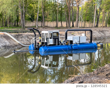 A specialized water management vessel works diligently on a calm pond, managing water levels and ensuring environmental care on a sunny day A specialized water management vessel works diligently on a calm pond, managing water levels and ensuring environmental care on a sunny day 128545321