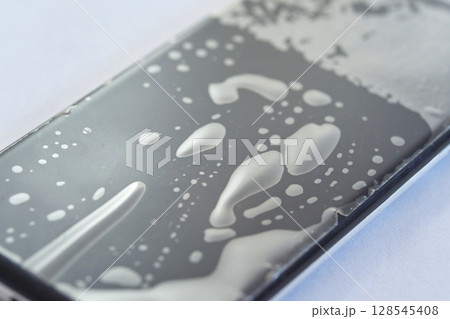 Close-up of water droplets on smartphone screen with abstract pattern on surface 128545408