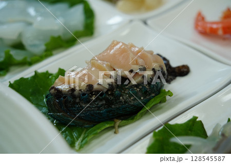 Fresh Abalone Sashimi Slices on White Plate with Green Leaf Garnish Fresh Abalone Sashimi Slices on White Plate with Green Leaf Garnish 128545587