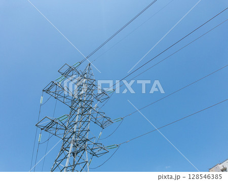 Electric power transmission towers with high-voltage lines against clear blue sky, metal lattice structures for energy distribution, industrial infrastructure in outdoor urban environment Electric power transmission towers with high-voltage lines against clear blue sky, metal lattice structures for energy distribution, industrial infrastructure in outdoor urban environment 128546385
