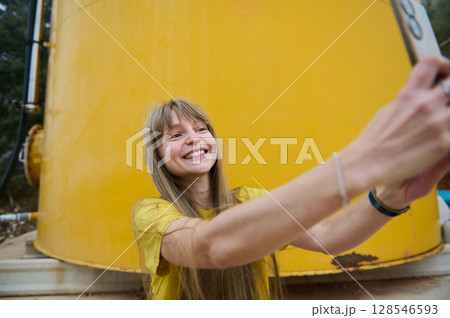 Smiling Woman Taking a Selfie in Front of a Bright Yellow Tank in an Outdoor Setting Smiling Woman Taking a Selfie in Front of a Bright Yellow Tank in an Outdoor Setting 128546593