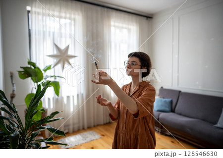 Calm woman lighting palo santo stick, fill home with aromatic smoke to create cozy atmosphere Calm woman lighting palo santo stick, fill home with aromatic smoke to create cozy atmosphere 128546630