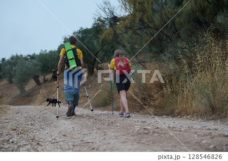 Young Couple Hiking in Nature With Trekking Sticks and Dog Through Scenic Outdoors 128546826