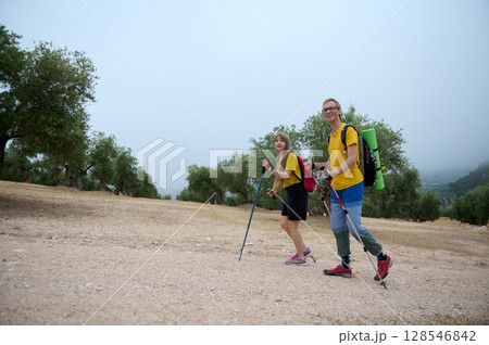 Young Couple Hiking Through Scenic Mountain Trails with Trekking Sticks and Backpacks Young Couple Hiking Through Scenic Mountain Trails with Trekking Sticks and Backpacks 128546842