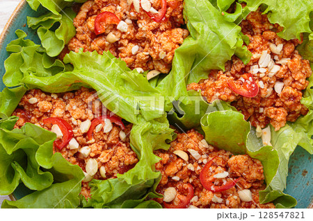Lettuce wraps filled with minced meat and topped with peanuts and chili pepper flakes on a plate, healthy protein dish 128547821