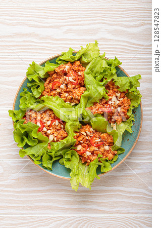Lettuce wraps filled with minced meat and topped with peanuts and chili pepper flakes on a plate, healthy protein dish 128547823