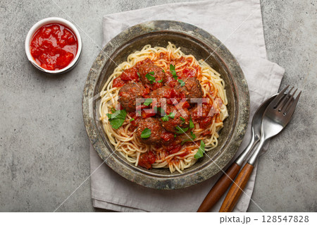 Spaghetti and meatballs with tomato sauce served on rustic plate with cutlery top view, Italian cuisine 128547828
