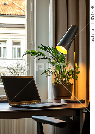 A laptop is on a desk next to a plant 128548340