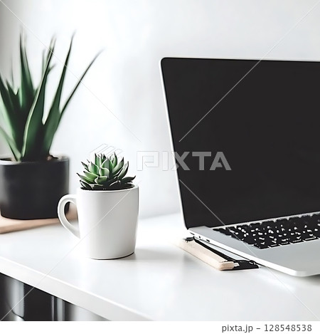 A white laptop sits on a table next to a potted plant and a white coffee cup 128548538