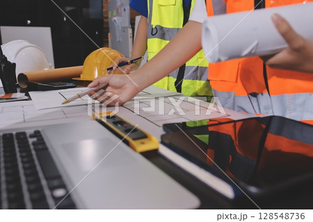 Closeup of team of industrial engineers meeting analyze machinery blueprints consult project on table in manufacturing factory. Working in manufacturing plant or production plant. 128548736