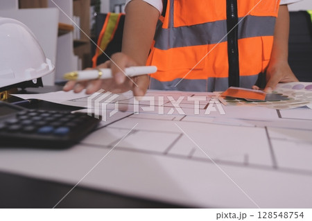 Closeup of team of industrial engineers meeting analyze machinery blueprints consult project on table in manufacturing factory. Working in manufacturing plant or production plant. Closeup of team of industrial engineers meeting analyze machinery blueprints consult project on table in manufacturing factory. Working in manufacturing plant or production plant. 128548754