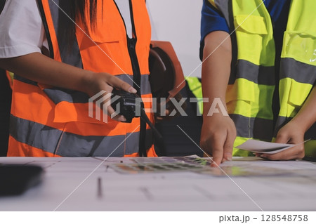 Closeup of team of industrial engineers meeting analyze machinery blueprints consult project on table in manufacturing factory. Working in manufacturing plant or production plant. Closeup of team of industrial engineers meeting analyze machinery blueprints consult project on table in manufacturing factory. Working in manufacturing plant or production plant. 128548758