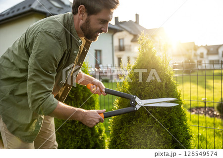 Young caucasian man cutting bushes with a prune in the garden Young caucasian man cutting bushes with a prune in the garden 128549574