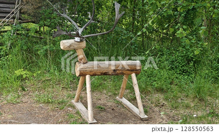 Handcrafted wooden deer toy with real antlers standing on grass near a forest background 128550563