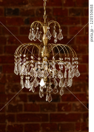Gold chandelier with crystal drops against brick wall background 128550688