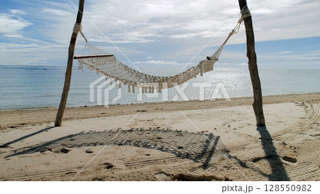 Soft waves touch the shore as a hammock shifts gently between posts on a peaceful beach in the Philippines Soft waves touch the shore as a hammock shifts gently between posts on a peaceful beach in the Philippines 128550982