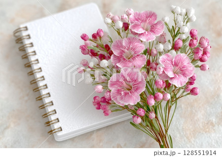 White notebook mockup with pink and white flowers arranged on a marble surface, perfect for feminine stationery or branding design presentations. 128551914