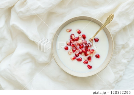 Minimalist bowl of coconut milk with muted pomegranate seeds, styled in soft creamy tones on textured linen for a serene modern food concept. 128552296