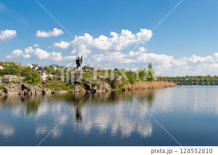 green coast of a beautiful small river with white clouds in reflection 128552810