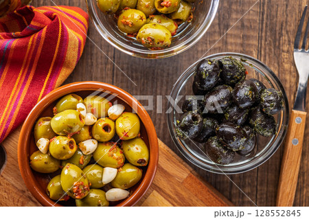 Tapas. Flavored pickled olives in bowl on wooden table. Top view. 128552845