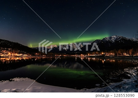 Northern lights illuminating snowy mountain and reflecting in calm lake at night 128553090