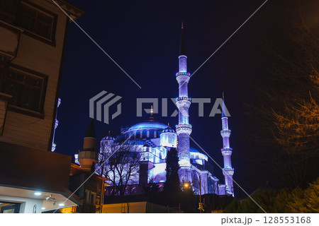 The Blue Mosque's domes and six minarets glow under night lighting, surrounded by nearby buildings and trees, showcasing its iconic architecture. 128553168