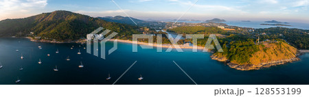 Aerial view of Naiharn Beach in Phuket, Thailand, showing turquoise waters with sailboats, lush green hills, and a hilltop structure in the distance. Aerial view of Naiharn Beach in Phuket, Thailand, showing turquoise waters with sailboats, lush green hills, and a hilltop structure in the distance. 128553199