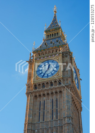Elizabeth Tower, known as Big Ben, stands tall in London, England. The Gothic Revival architecture is highlighted, featuring detailed stonework and a large clock face. 128553275