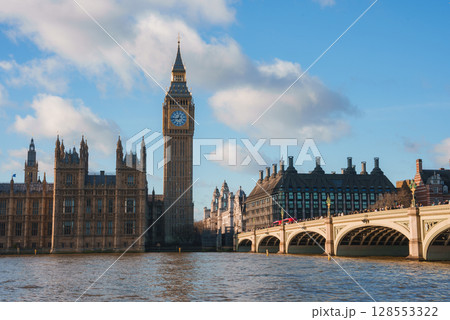 View of Big Ben and the Houses of Parliament in London, England, with Westminster Bridge and a red double decker bus crossing the River Thames. 128553322