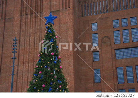A large Christmas tree with colorful ornaments and a blue star stands before the Tate Modern's red brick facade and grid like windows in London. A large Christmas tree with colorful ornaments and a blue star stands before the Tate Modern's red brick facade and grid like windows in London. 128553327