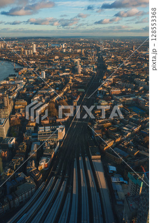 Aerial view of London during Christmas, featuring railway tracks, the River Thames, and city landmarks under a partly cloudy, golden sky. 128553368
