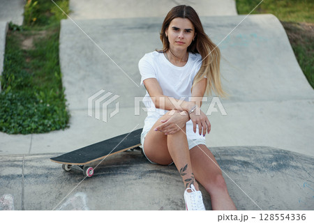 Fashion pretty hipster girl with skateboard on skate park sitting on the ramp. Fashion pretty hipster girl with skateboard on skate park sitting on the ramp. 128554336