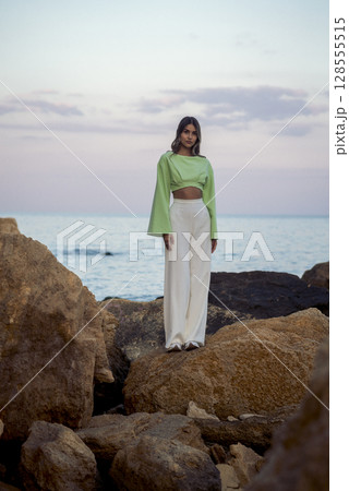 a slender young girl in white trousers stands on the seashore 128555515