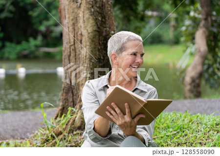 Senior Woman Enjoying a Book Outdoors in a Park by a Lake on a Sunny Day Senior Woman Enjoying a Book Outdoors in a Park by a Lake on a Sunny Day 128558090